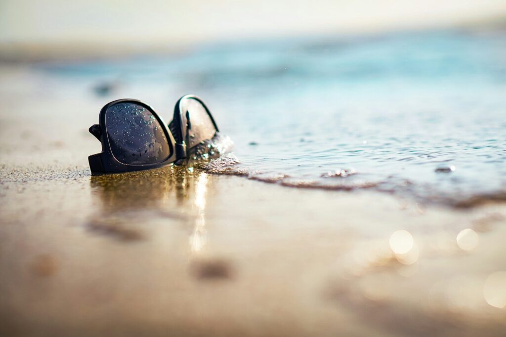 Sunglasses rest on the beach near the water.